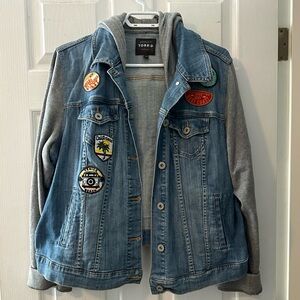 Torrid denim jacket with patches, hood, and sweatshirt style sleeves.